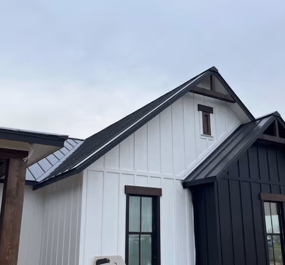 Modern house exterior with white and dark gray vertical siding and black metal roofs under a cloudy sky.