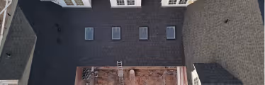 Aerial view of a rooftop with five skylights, adjacent to a construction site with exposed ground and building materials.