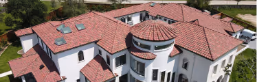 Aerial view of a large white house with multiple sections of red tiled roofs and skylights.