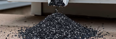 Black granules or pellets falling from a white chute forming a pile on the floor.