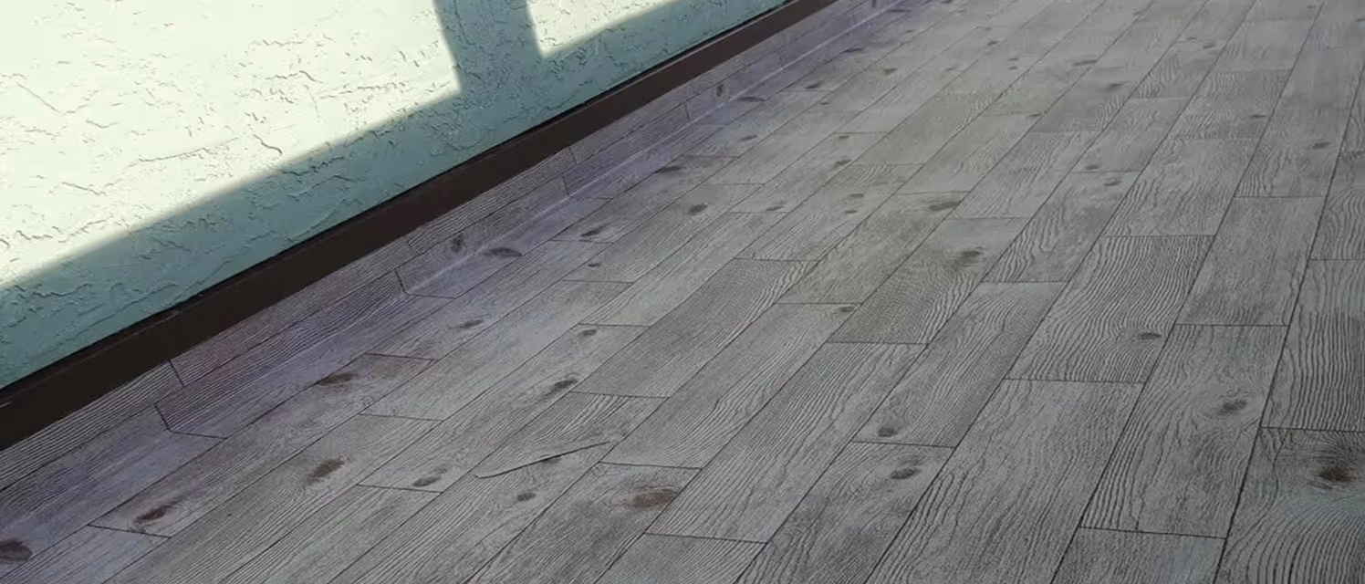Balcony floor with weathered wood-patterned tiles and a textured light green wall casting a shadow.