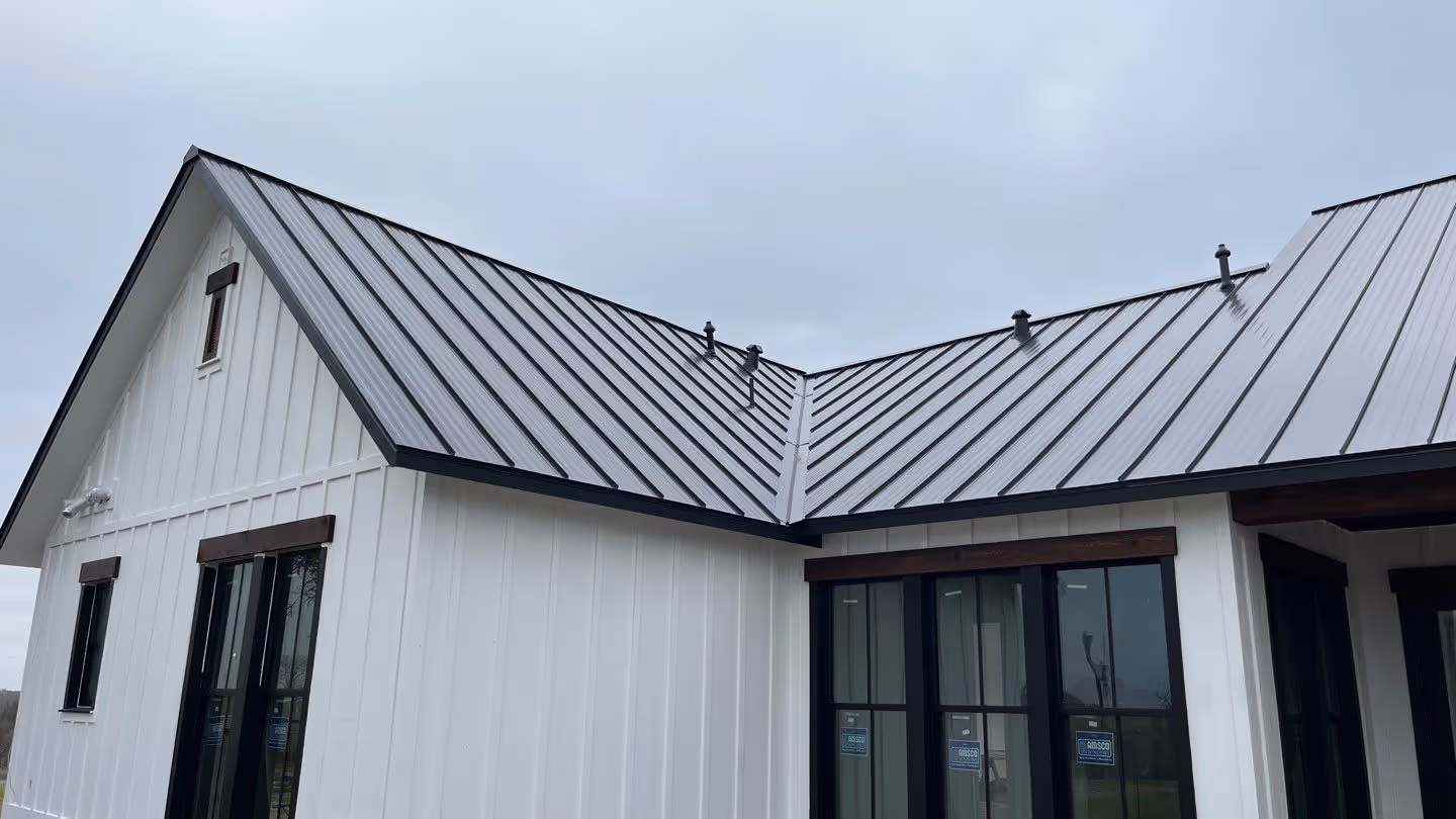 White house exterior with black metal standing seam roof and large windows under a cloudy sky.