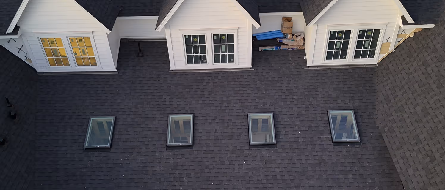 Four rectangular skylights installed in a dark shingled roof beneath three white dormer windows with double-hung panes.