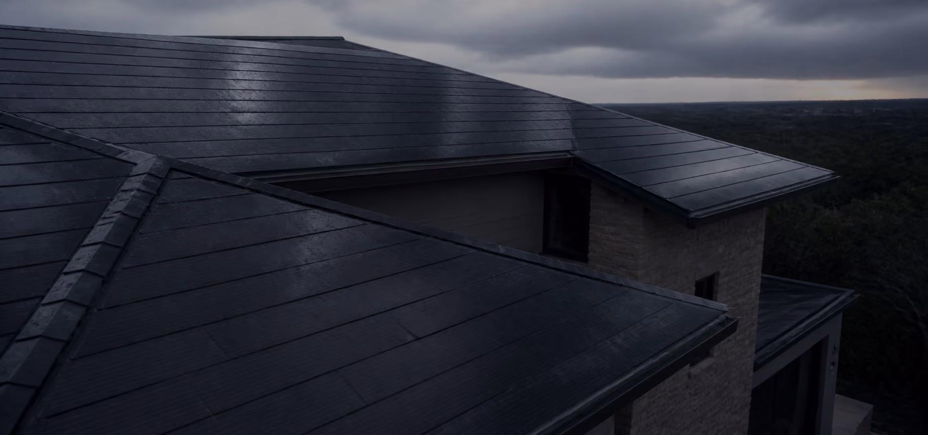Modern house roof with dark solar tiles under cloudy sky during dusk.