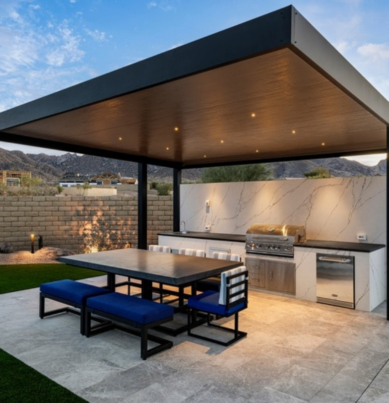 Shade ramada with outdoor kitchen and dining table on a paver patio with artificial turf by Kevens Landscape