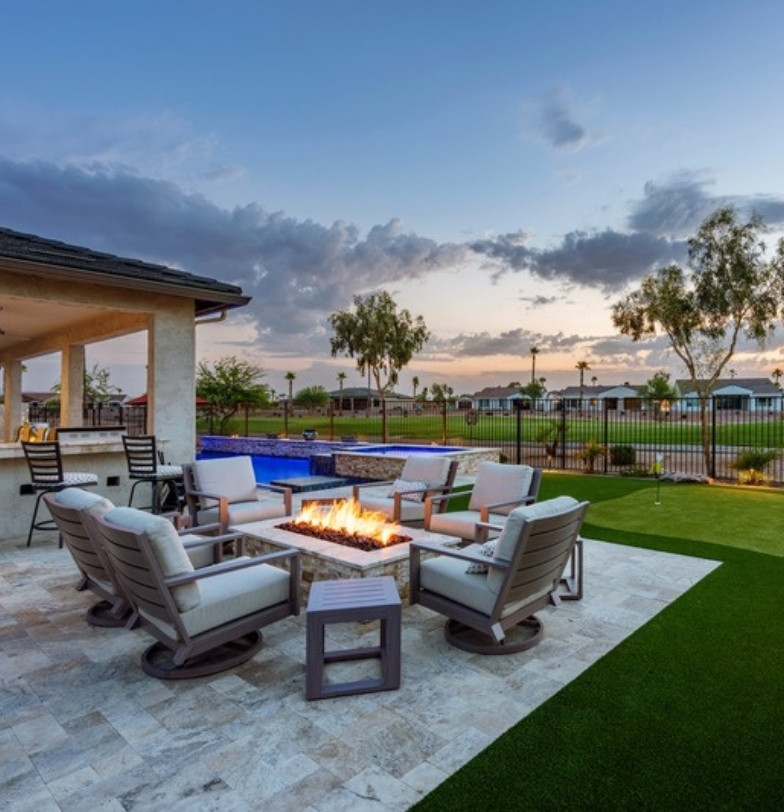 Travertine patio with fire pit seating, pool and green turf at sunset by Kevens Landscape
