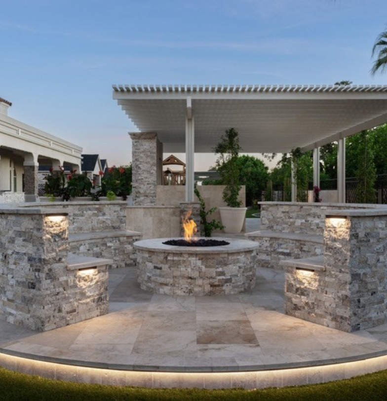 Circular stone fire pit with seating walls and patio cover in a green backyard by Kevens Landscape