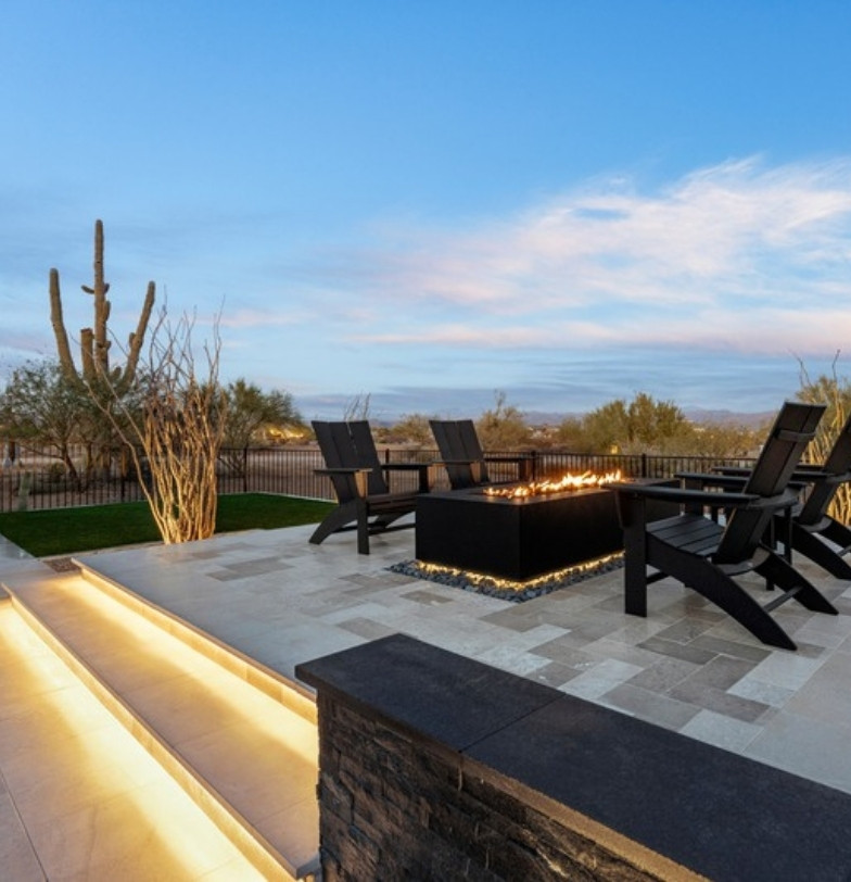 Raised paver patio with fire pit and chairs overlooking open desert and a saguaro by Kevens Landscape