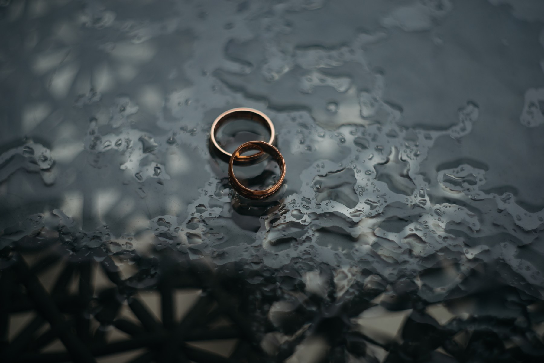 Two gold rings on a wet, reflective surface with blurred patterns in the background. The mood is serene and contemplative.