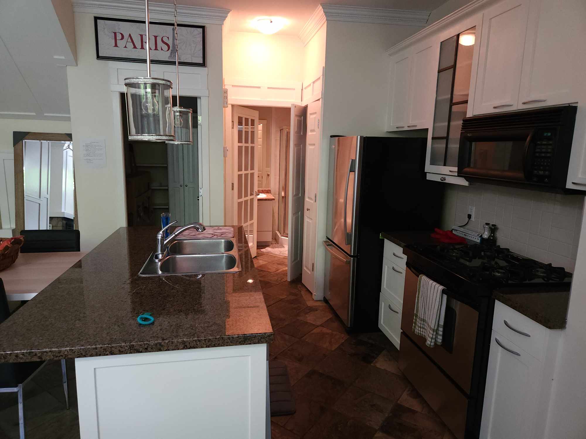 Modern kitchen with granite countertops, stainless steel refrigerator and stove, white cabinets, and a dual sink island under pendant lights. Richard Street Townhouse: Urban Privacy in Yaletown