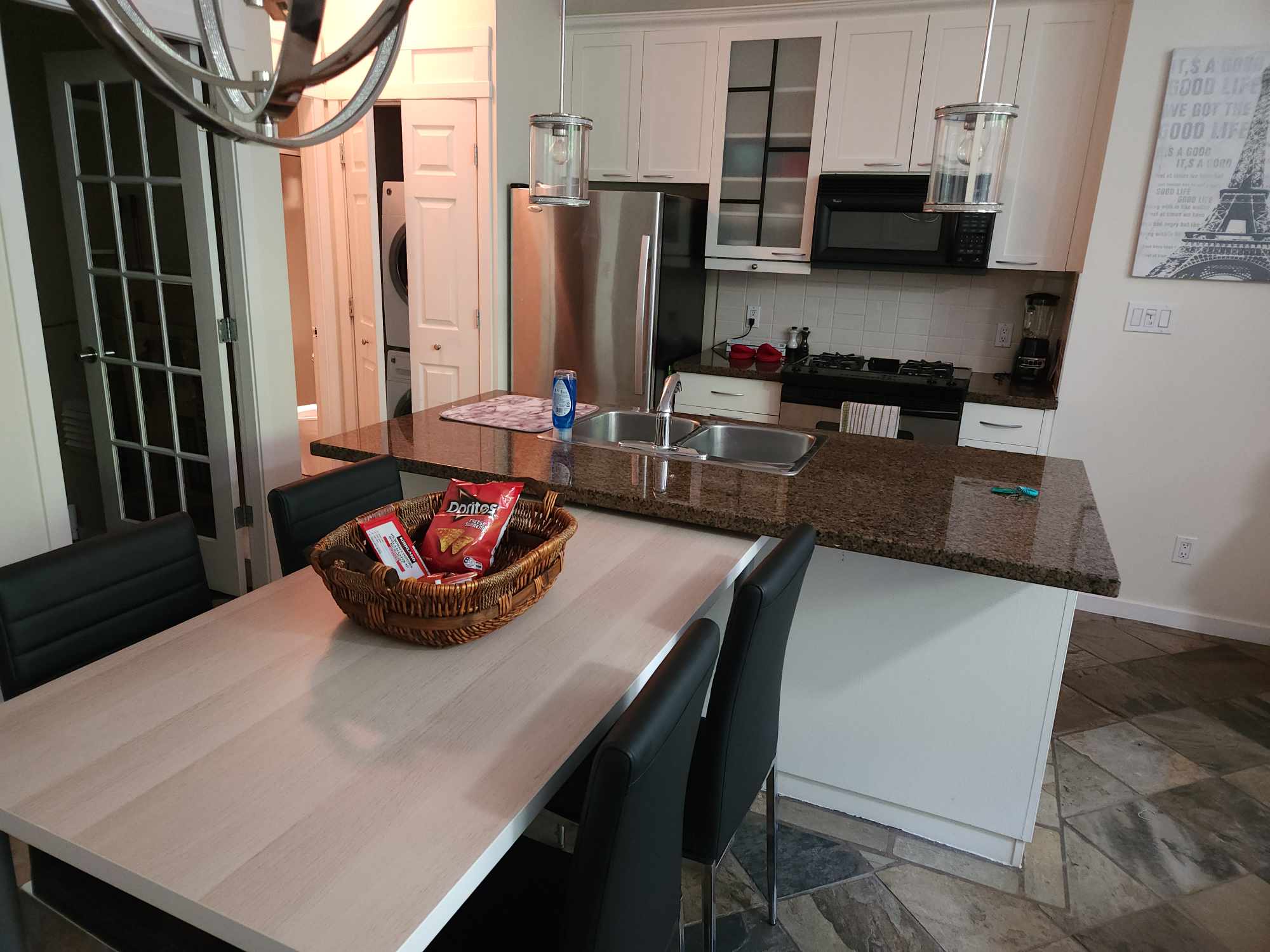 Modern kitchen with a granite countertop island, black leather chairs around a light wooden dining table, and a wicker basket containing snack bags on the table. Richard Street Townhouse: Urban Privacy in Yaletown