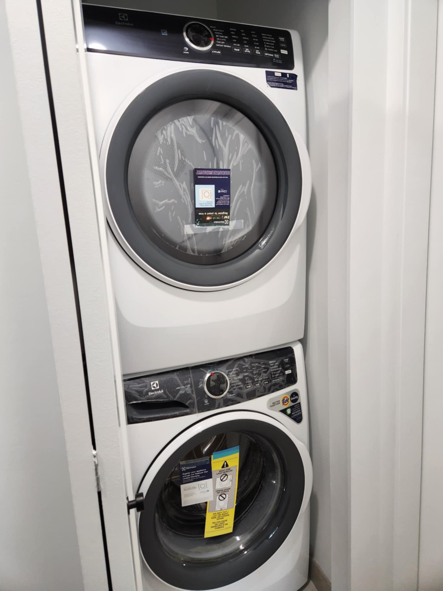 Stacked white Electrolux front-loading washer and dryer with labels on the doors inside a small laundry closet. Rupert Street Executive Retreat: Proximity & Peace