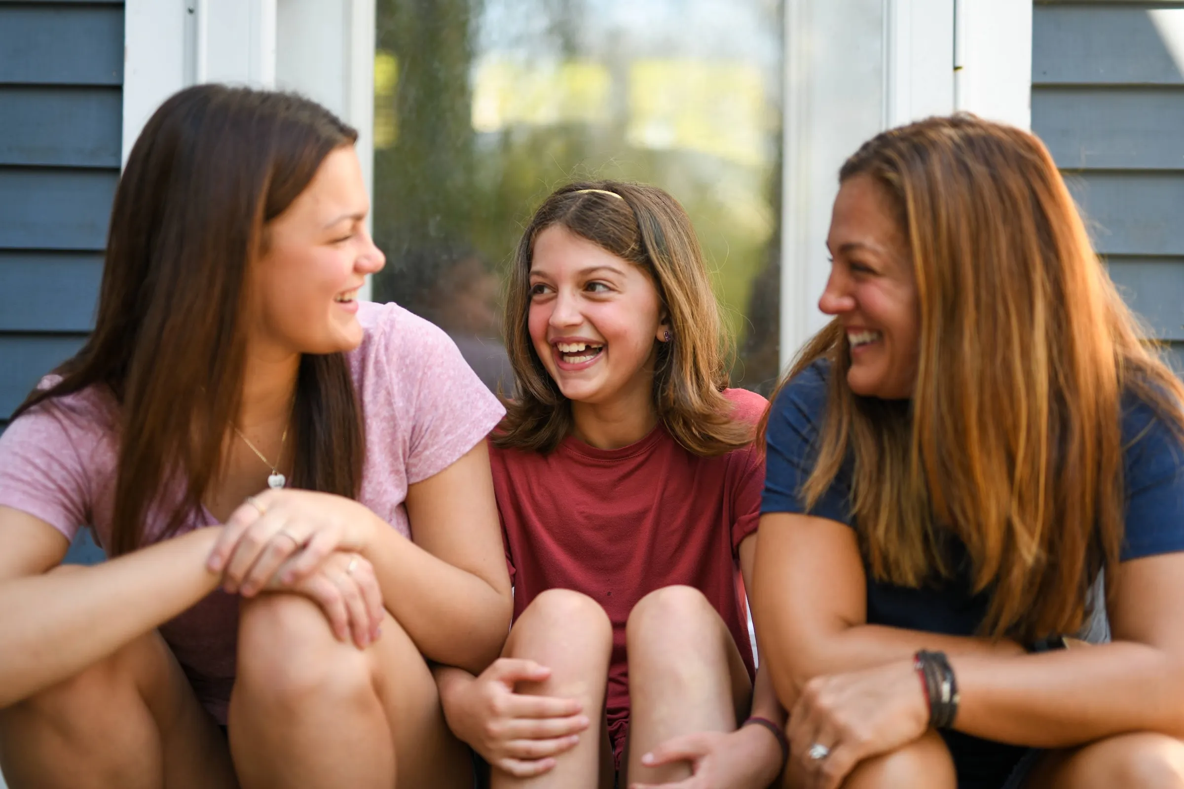 Three girls sitting together and laughing outdoors