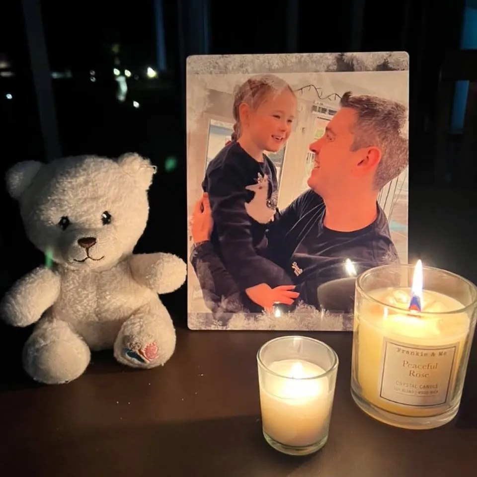 Memorial display with a framed photo, teddy bear, and lit candles