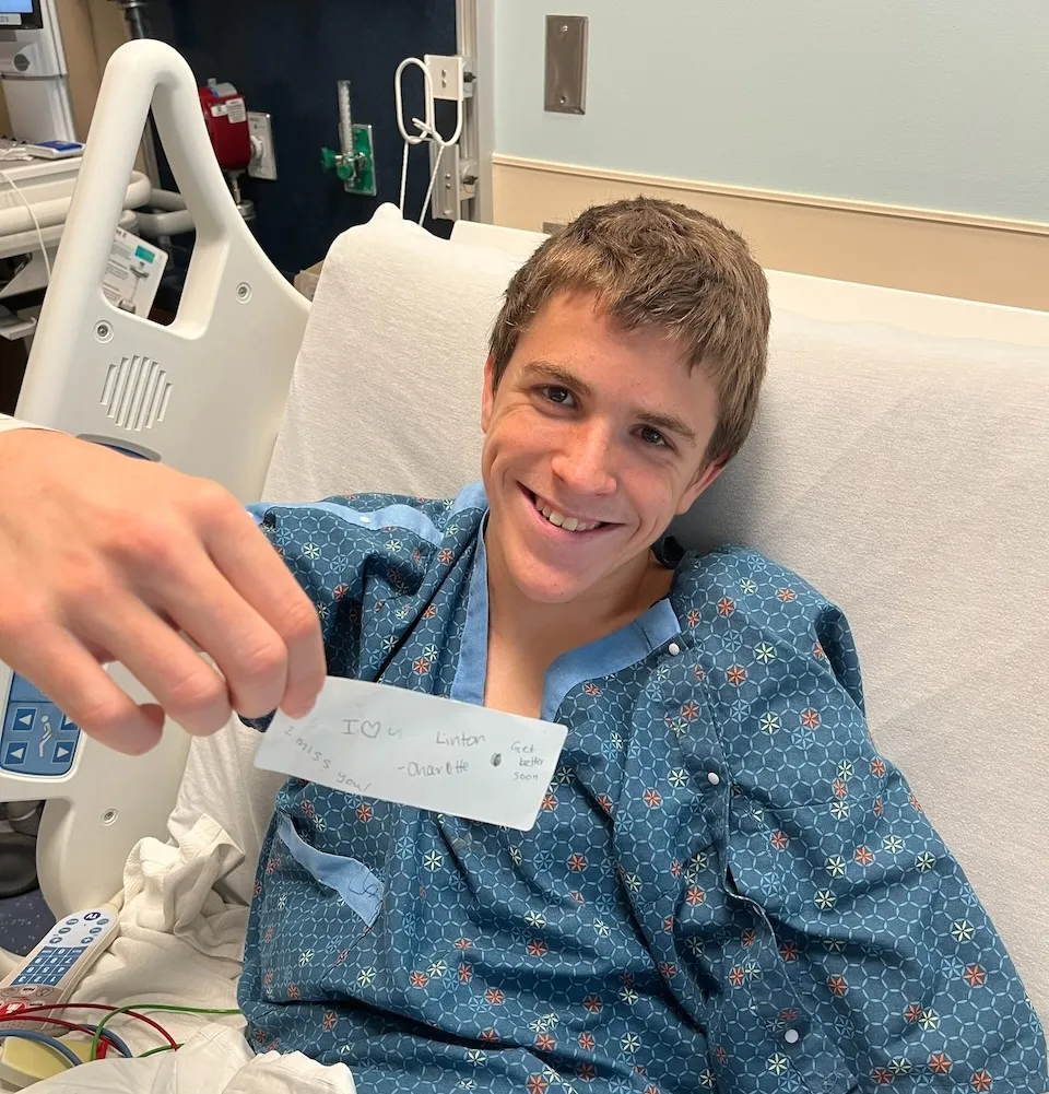 Young man smiling in a hospital bed while holding a handwritten note