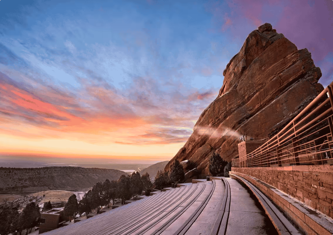 Curved amphitheater seating by large rock formation at sunset with pink and blue sky.