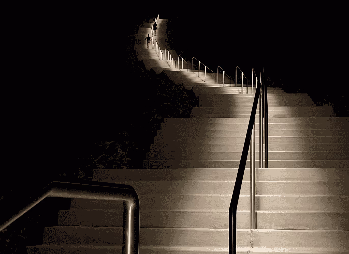 Long set of outdoor stairs lit at night with two people walking near the top.