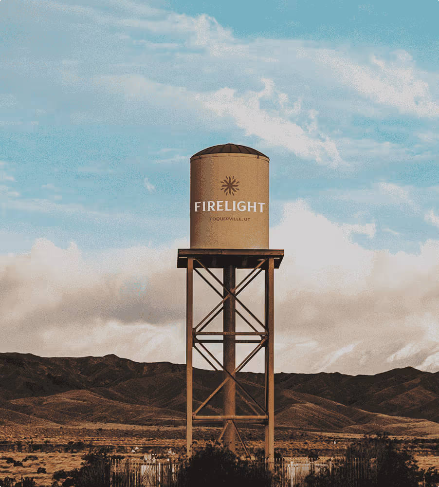 Firelight water tank on metal tower in a desert landscape with mountains and cloudy blue sky.