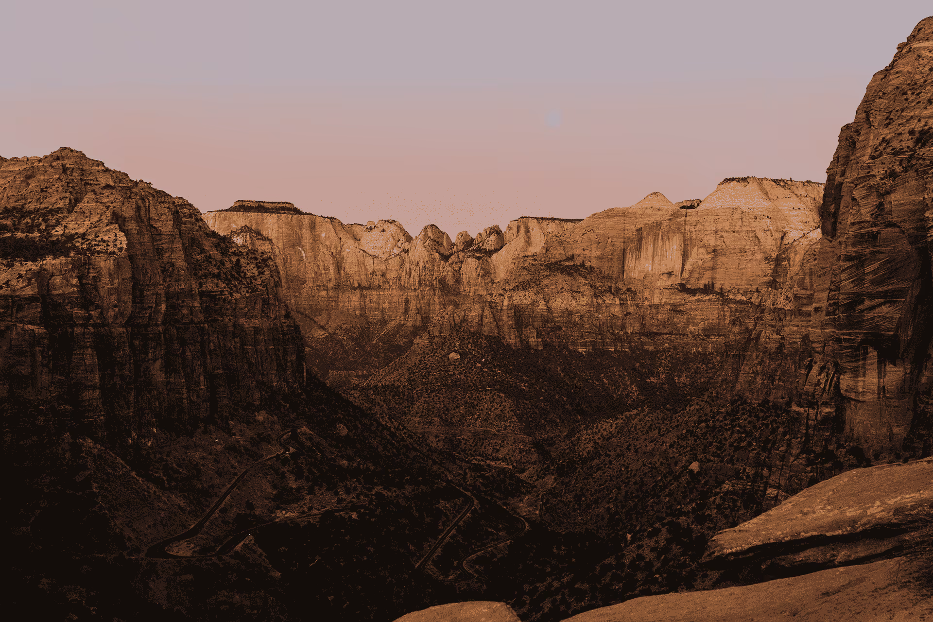 Wide canyon view with steep rocky cliffs under a clear sky at sunset or dusk.