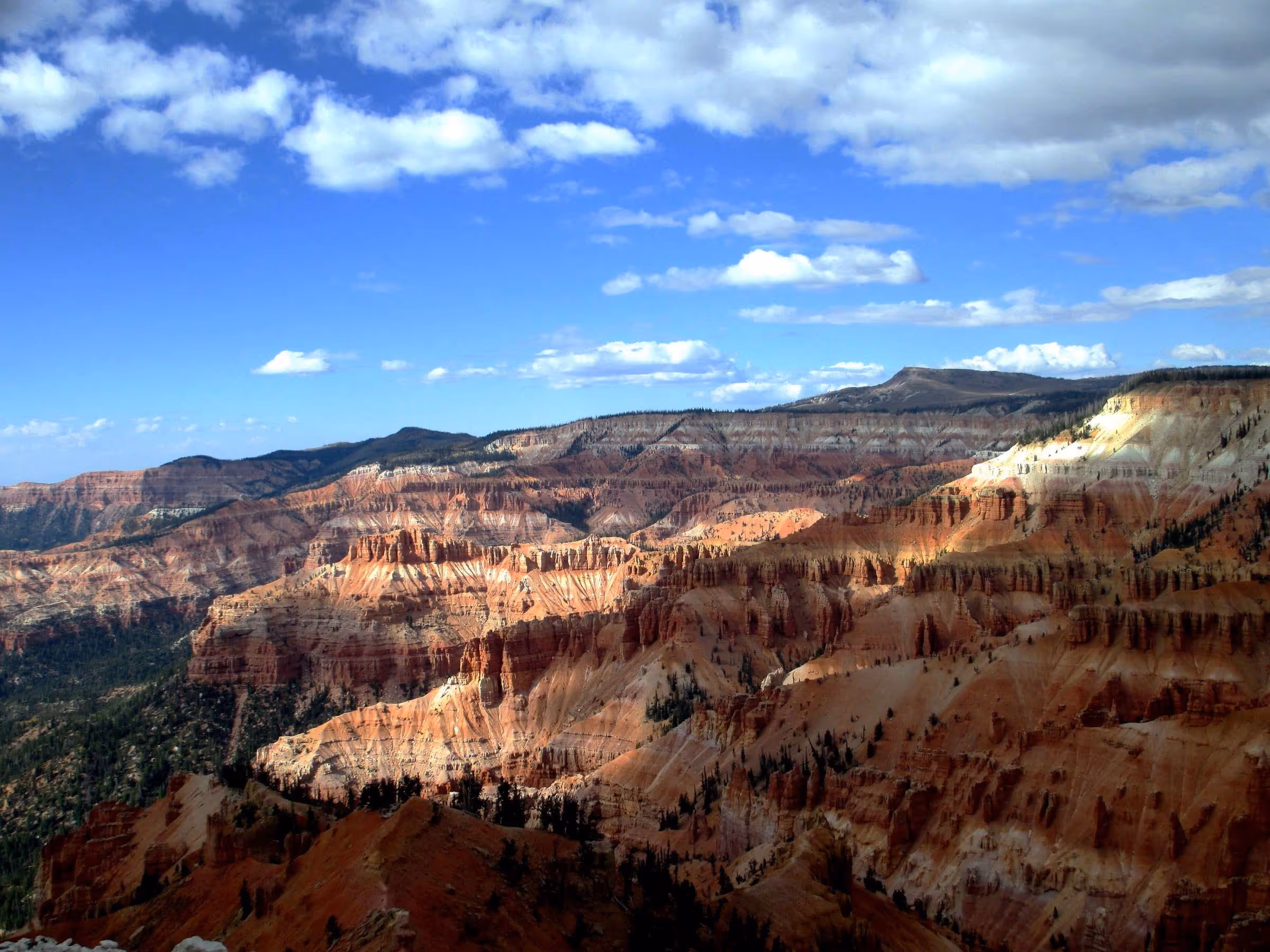 Layered red and white rock formations under a blue sky with scattered clouds in a canyon landscape.