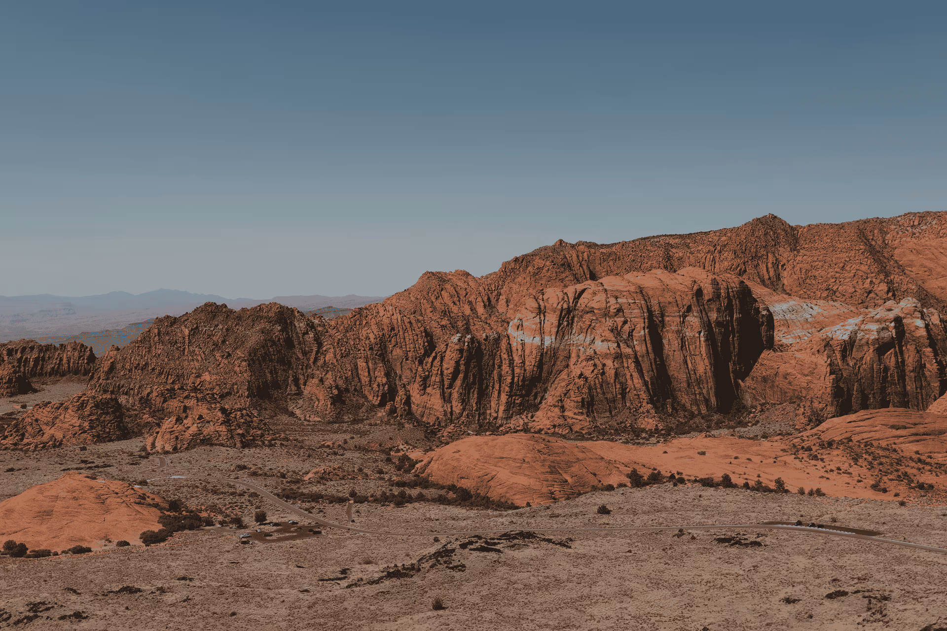Wide view of rocky red desert landscape with rugged cliffs under a clear blue sky.