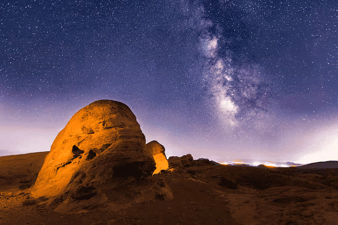 Starry night sky with the Milky Way over illuminated rocky desert landscape.