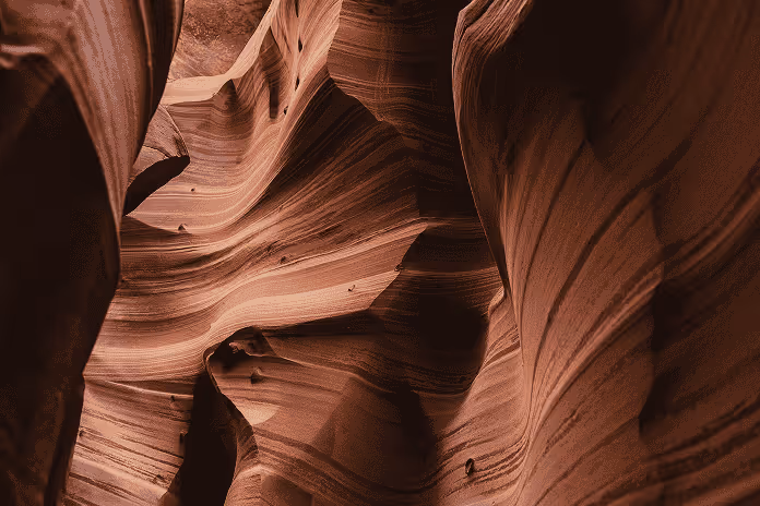 Wavy, layered sandstone canyon walls with light and shadow patterns inside a slot canyon.