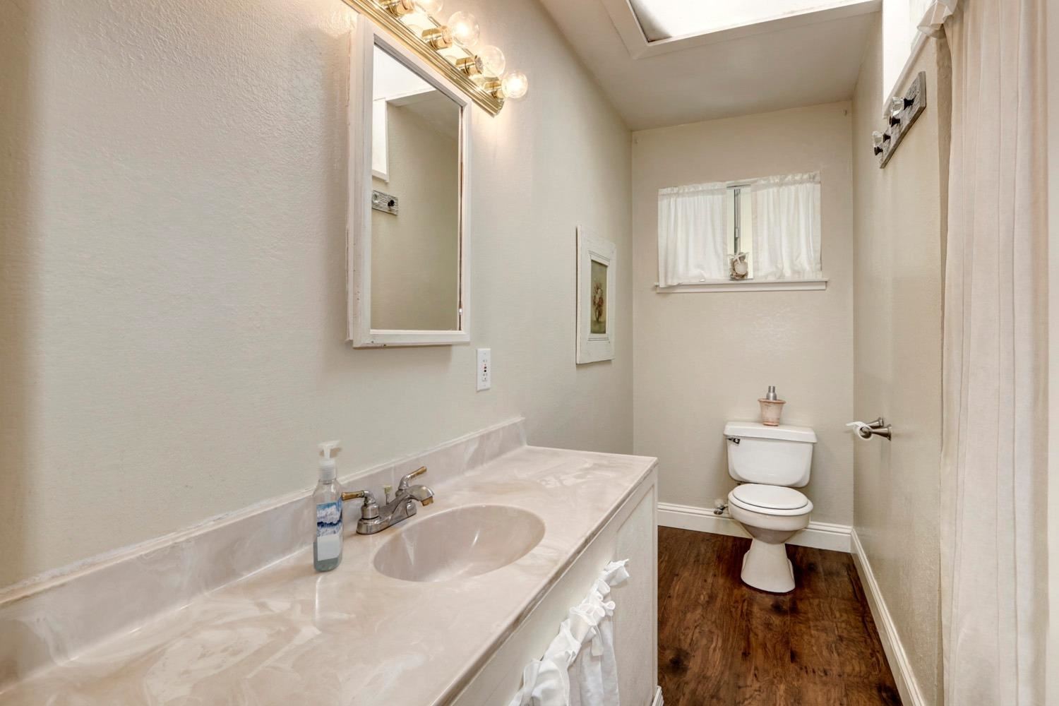 Narrow bathroom with beige countertop, single sink, mirror, toilet, and wood floor.