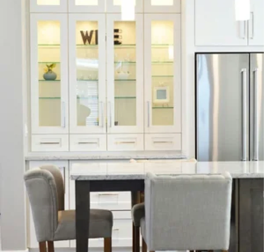 A grayscale photo showing white kitchen cabinets and a dining chair.