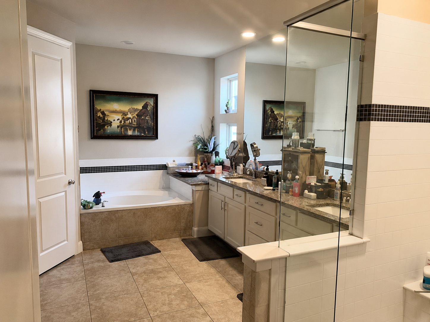 Modern Sacramento bathroom with a large bathtub, double sink vanity with cluttered countertop, tile flooring, and glass shower enclosure.