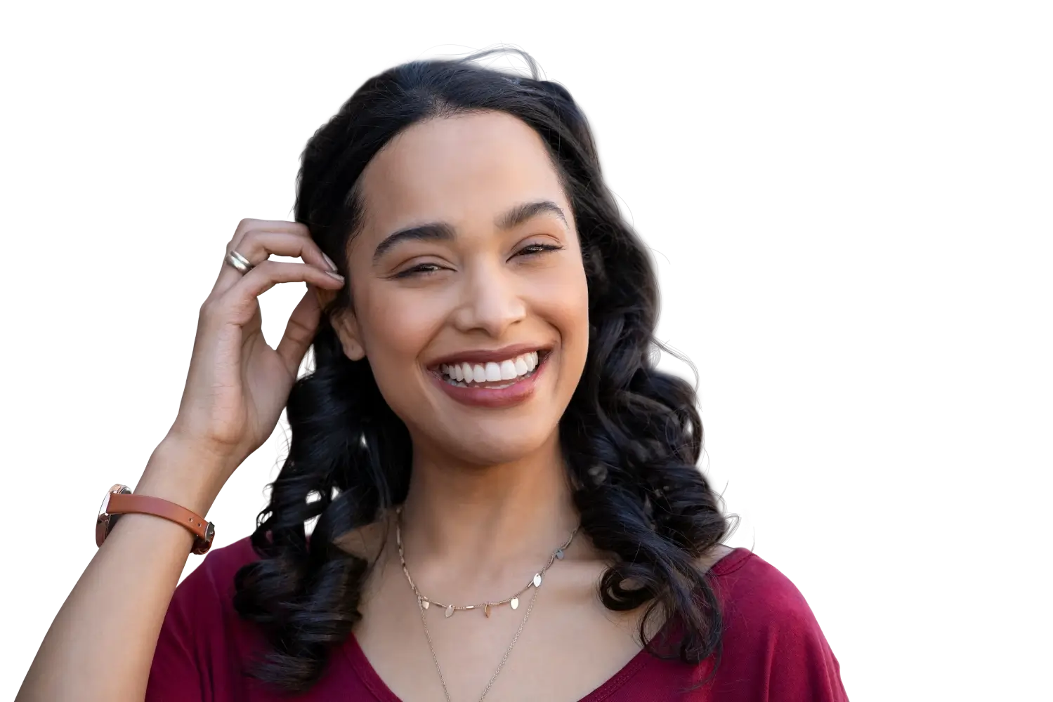 Smiling woman with curly hair wearing red top and jewelry, touching her hair near her ear.