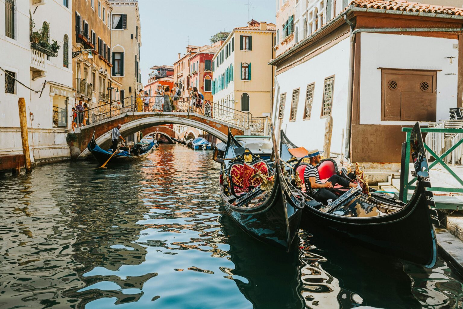 Gondolas with gondoliers and tourists on a canal under a bridge in Venice, Italy.