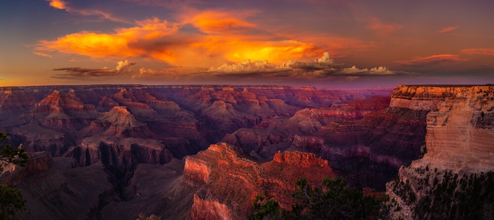 Sunset over Grand Canyon with glowing orange clouds and layered rock formations in purple and red hues.