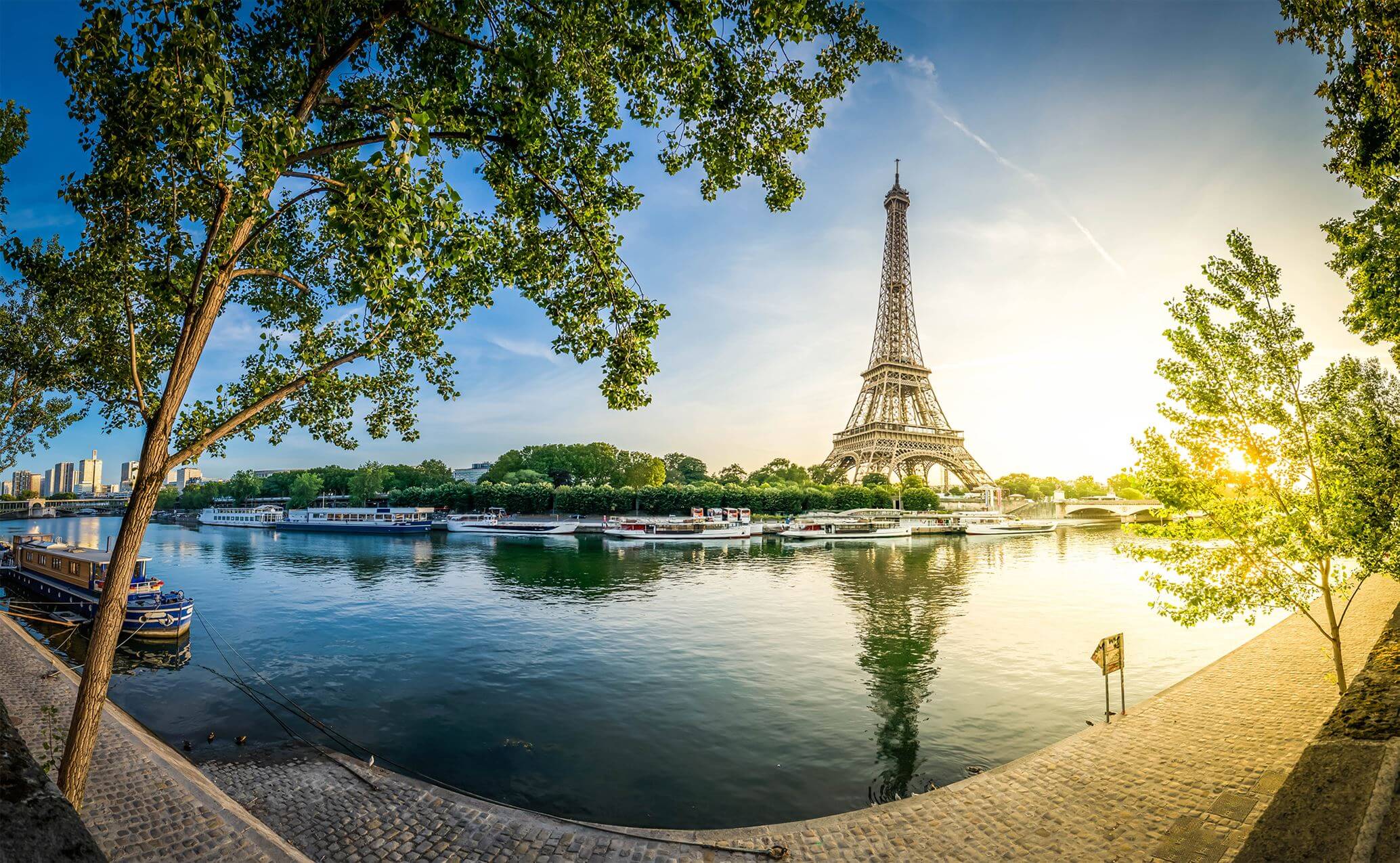 Eiffel Tower beside the Seine River with boats and trees at sunset in Paris.