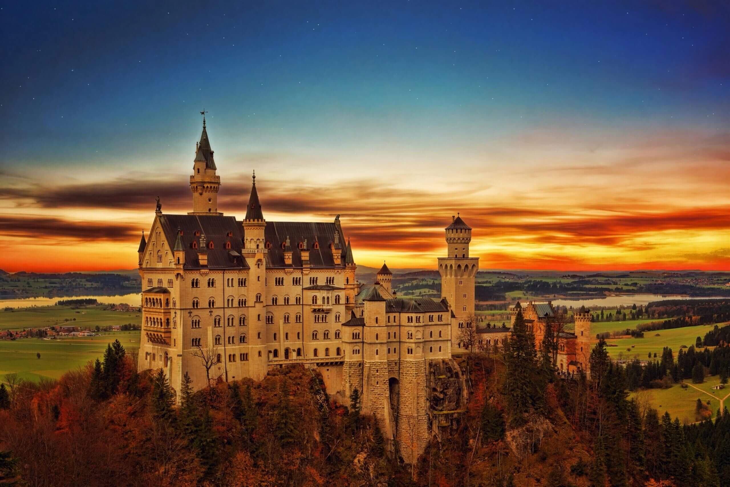 Neuschwanstein Castle on a hill with autumn trees at sunset under a starry sky.
