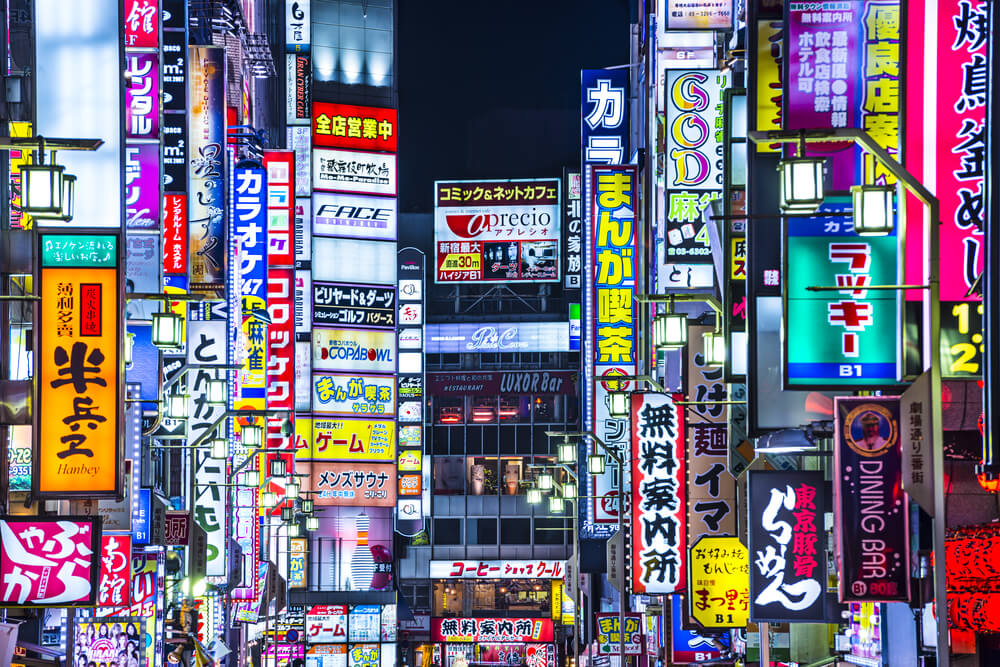 Colorful neon signs and billboards densely packed on buildings in a busy Japanese urban street at night.