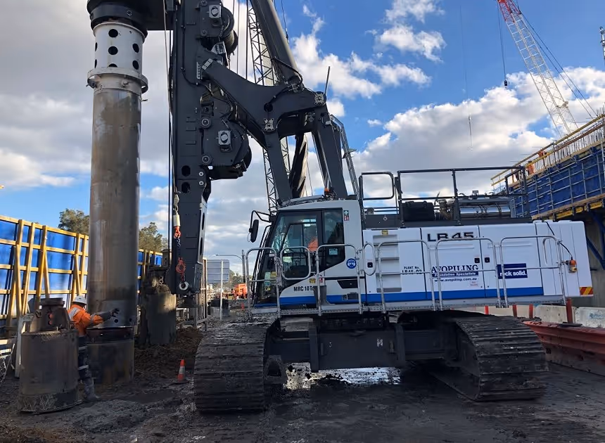 Grayscale group portrait of construction workers standing in front of heavy machinery.