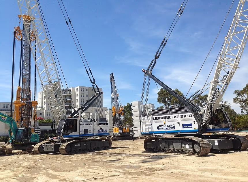 Grayscale group portrait of construction workers standing in front of heavy machinery.