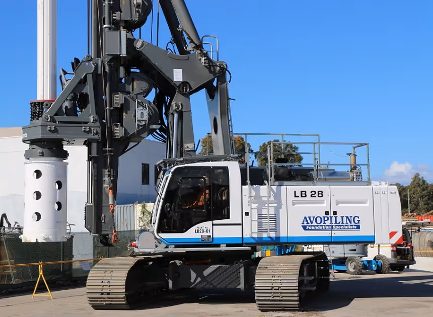 Grayscale group portrait of construction workers standing in front of heavy machinery.