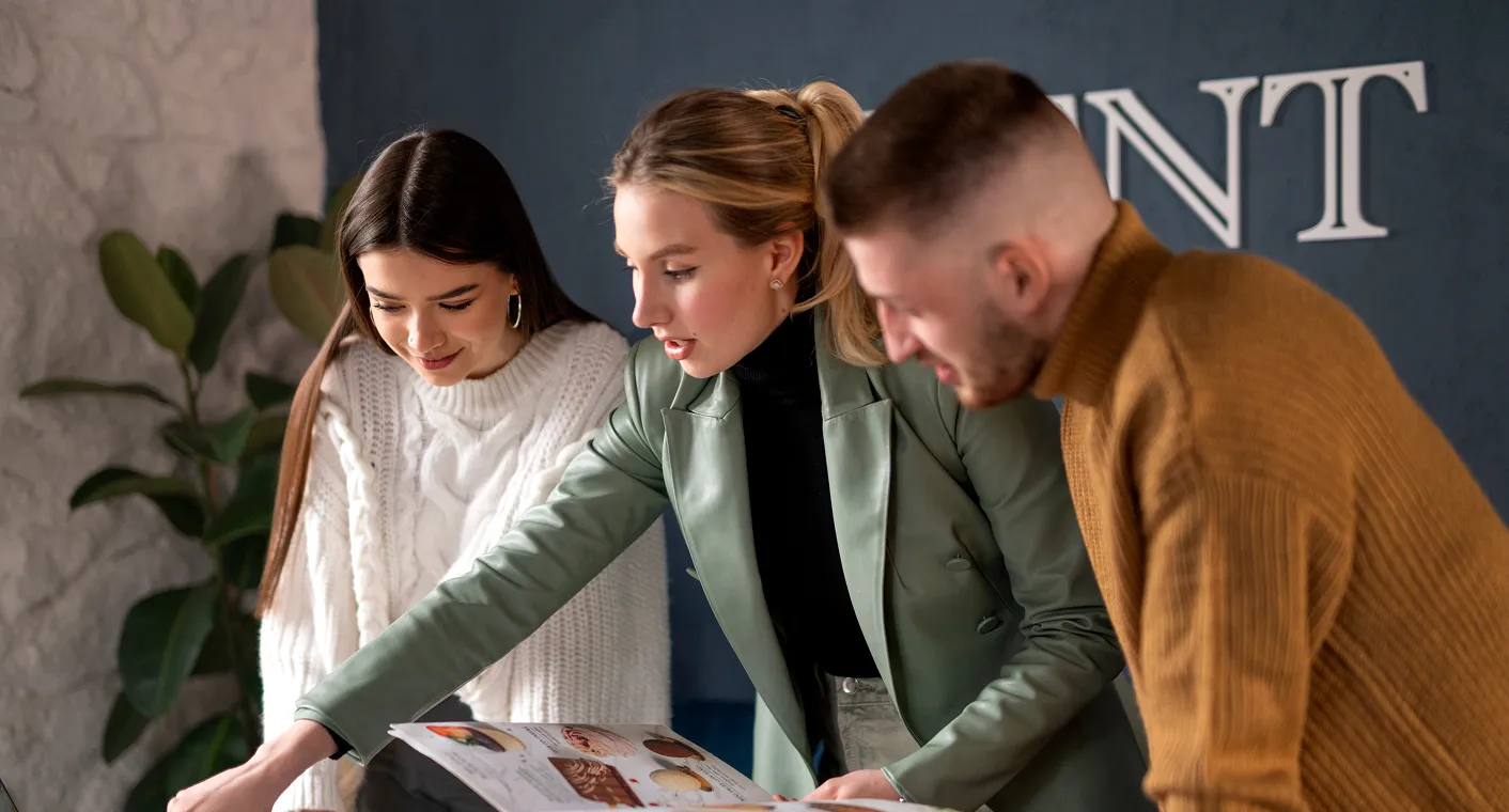 Three people, two women and one man, looking at a magazine together in an indoor setting.
