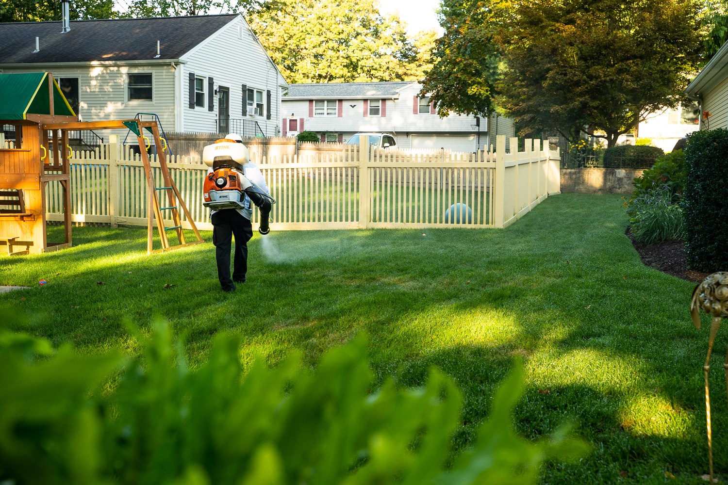 Mosquito Mike technician treating a fenced backyard beside a children's swing set