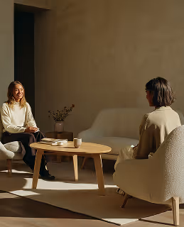 Two people seated in a bright, minimalist room with abundant natural light, showcasing refined spatial design and modern architectural aesthetics.