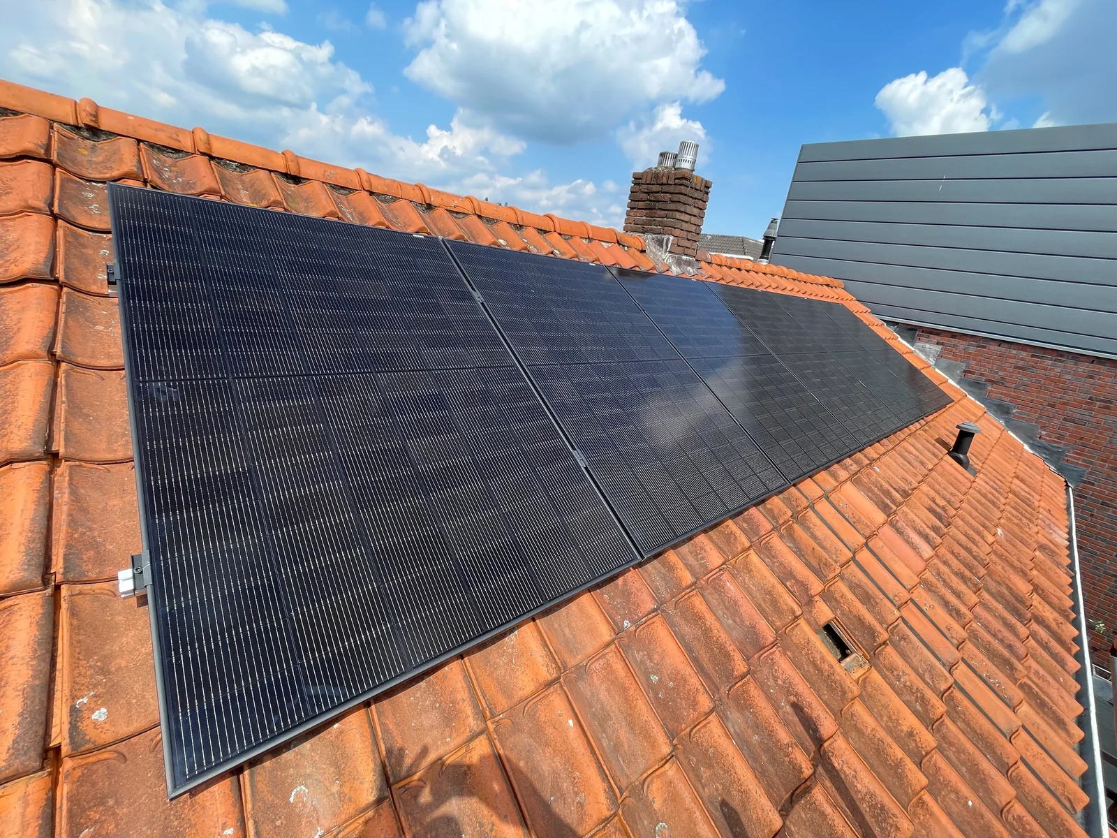 Zwarte zonnepanelen op een dak met rode dakpannen, aangelegd door ABGTGREEN