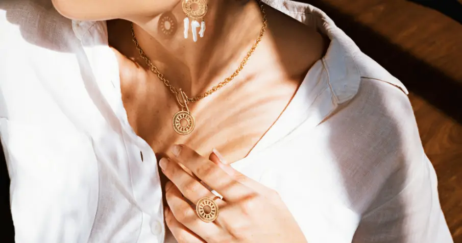 Woman wearing a gold chain necklace and holding another chain near her neck.