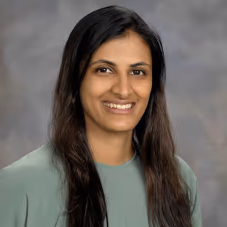 Smiling woman with long dark hair wearing a light green top against a gray background.