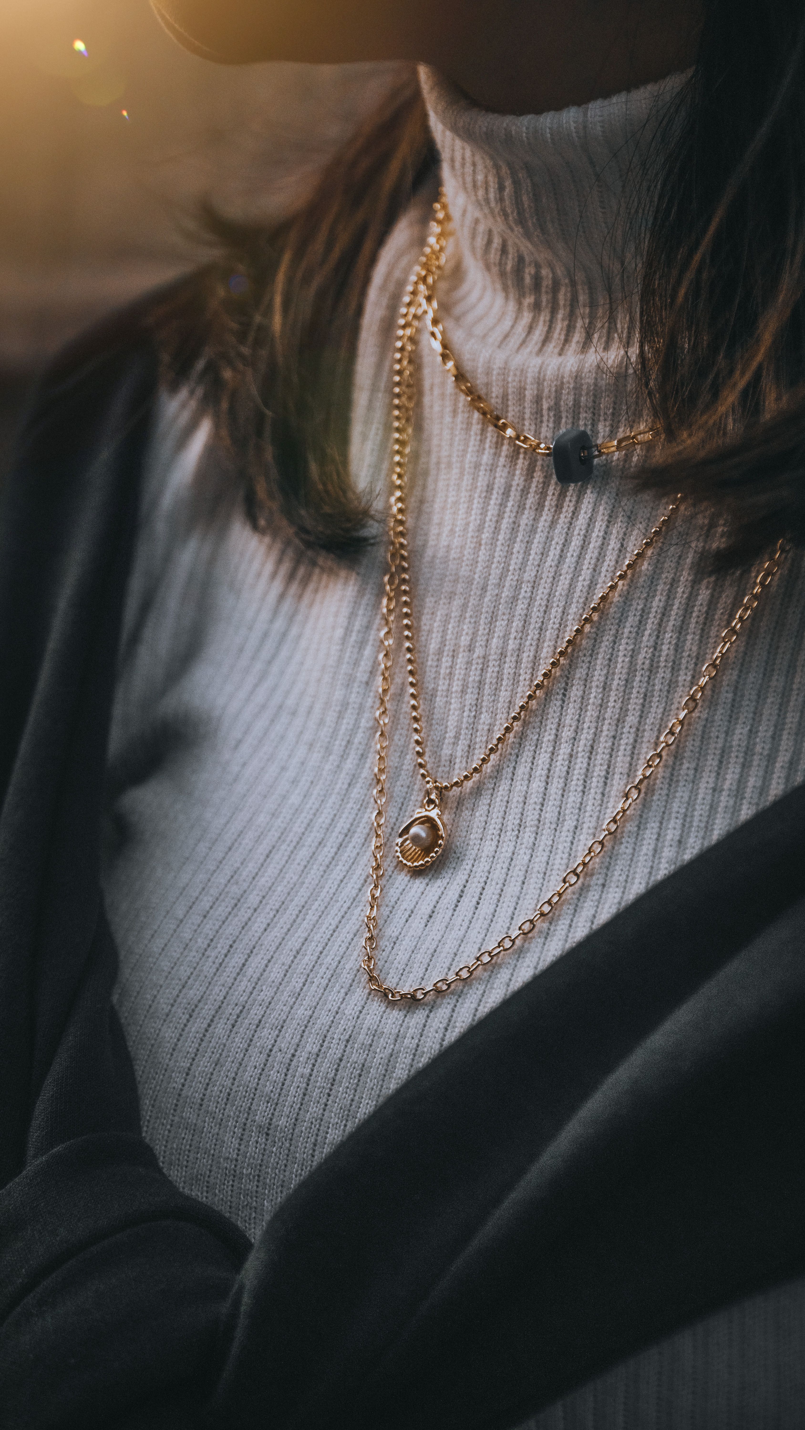 Woman wearing a gold chain necklace and holding another chain near her neck.