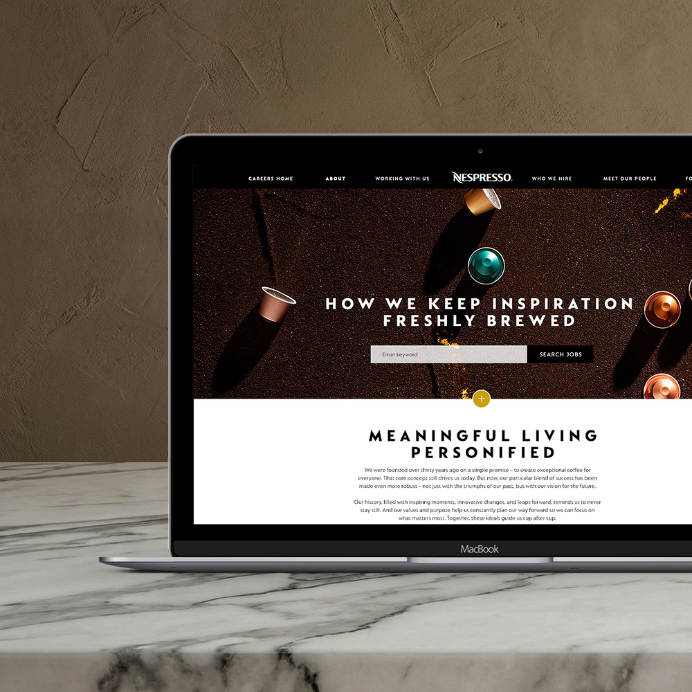 MacBook laptop on marble surface displaying a Nespresso careers webpage with coffee capsules and search bar.
