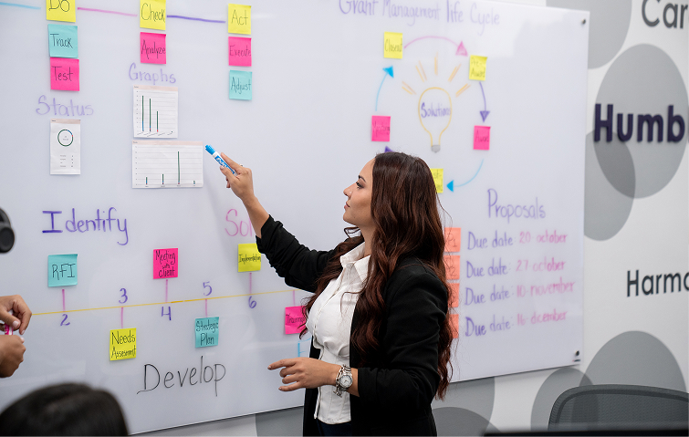 Two women in business attire working together on a laptop at a white conference table in a modern office.