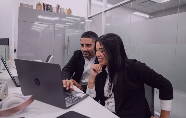 Two business colleagues sitting closely and smiling while looking at a laptop in a modern office.