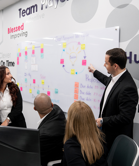 Business team in a meeting room with a man pointing at a whiteboard covered with sticky notes during a presentation.